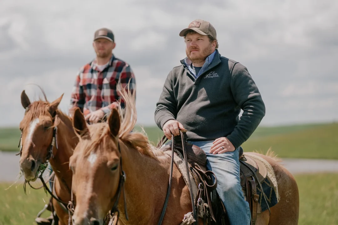 Two riders on horseback, one wearing a Topp Herefords vest